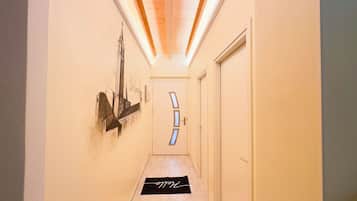 Un couloir étroit avec un plafond en bois, une porte ornée de motifs géométriques et un paillasson noir avec une inscription blanche.