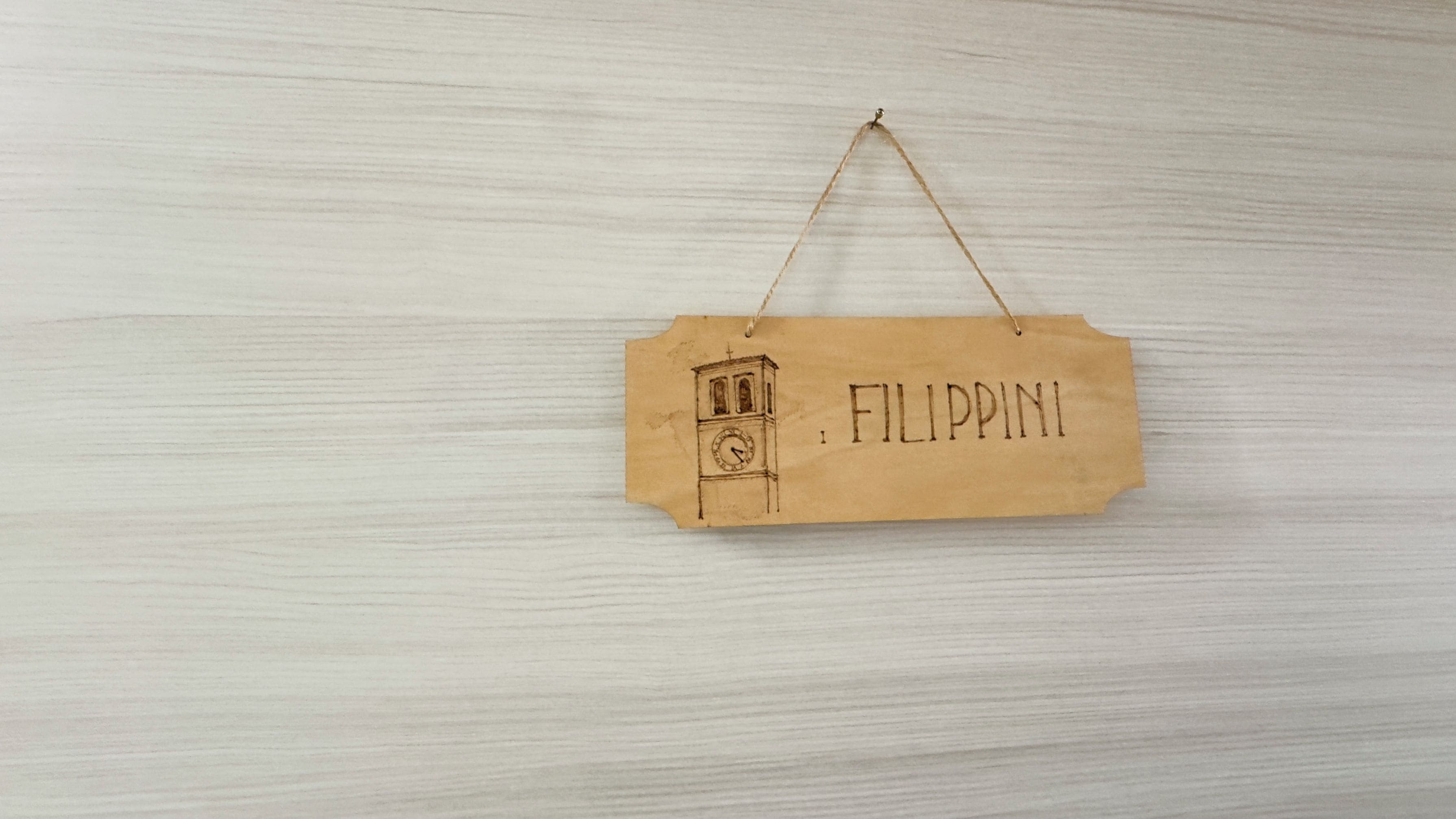 A wooden sign with a sketch of a clock tower and the word 'FILIPPINI' on a light wooden background.