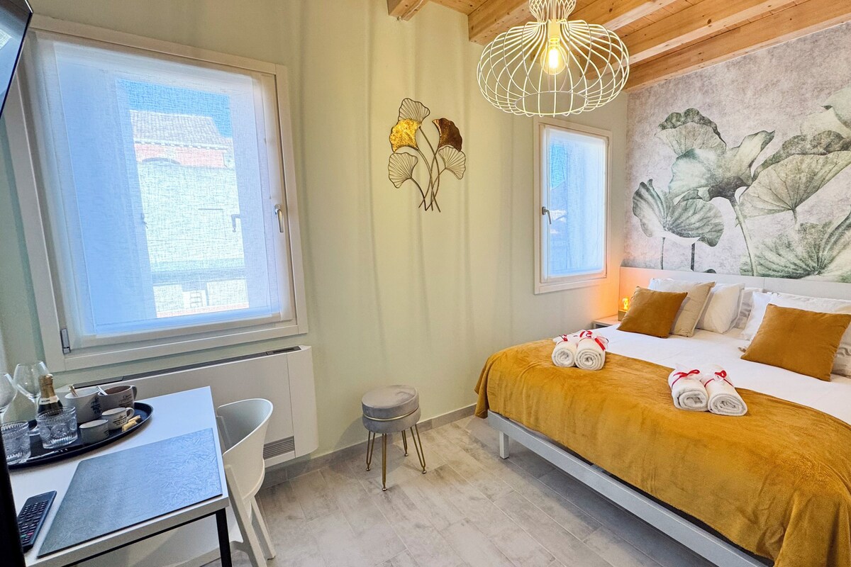 Ein Hotelzimmer mit einem Bett, einem Schreibtisch und einem Stuhl. Es gibt ein Fenster, eine Wanddekoration und eine Leuchte.