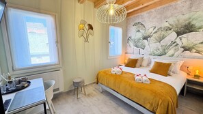 Ein Hotelzimmer mit einem Bett, einem Schreibtisch und einem Stuhl. Es gibt ein Fenster, eine Wanddekoration und eine Leuchte.
