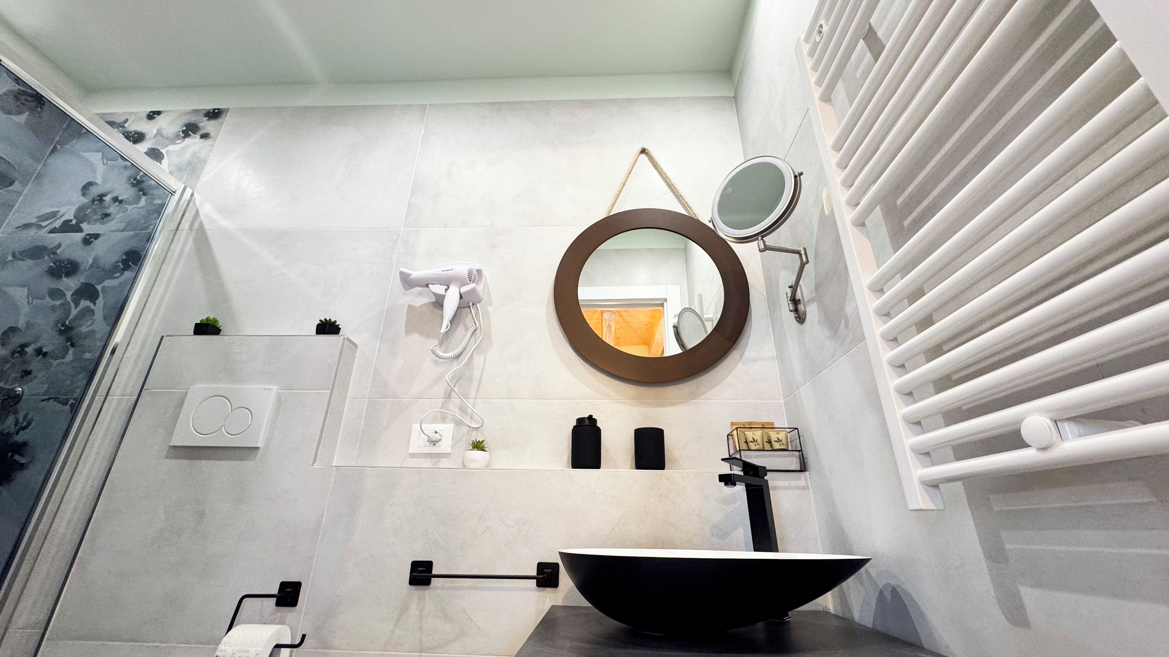 Une salle de bain moderne avec un lavabo noir, un miroir rond, un sèche-cheveux et un porte-serviettes.