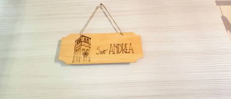 A wooden sign with a sketch of a tower and the name 'Sant' Andrea' on a light wooden surface.