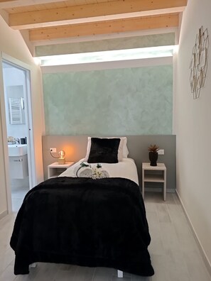 Un dormitorio con cama, mesitas de noche, lámpara de pared y vista de la habitación contigua.