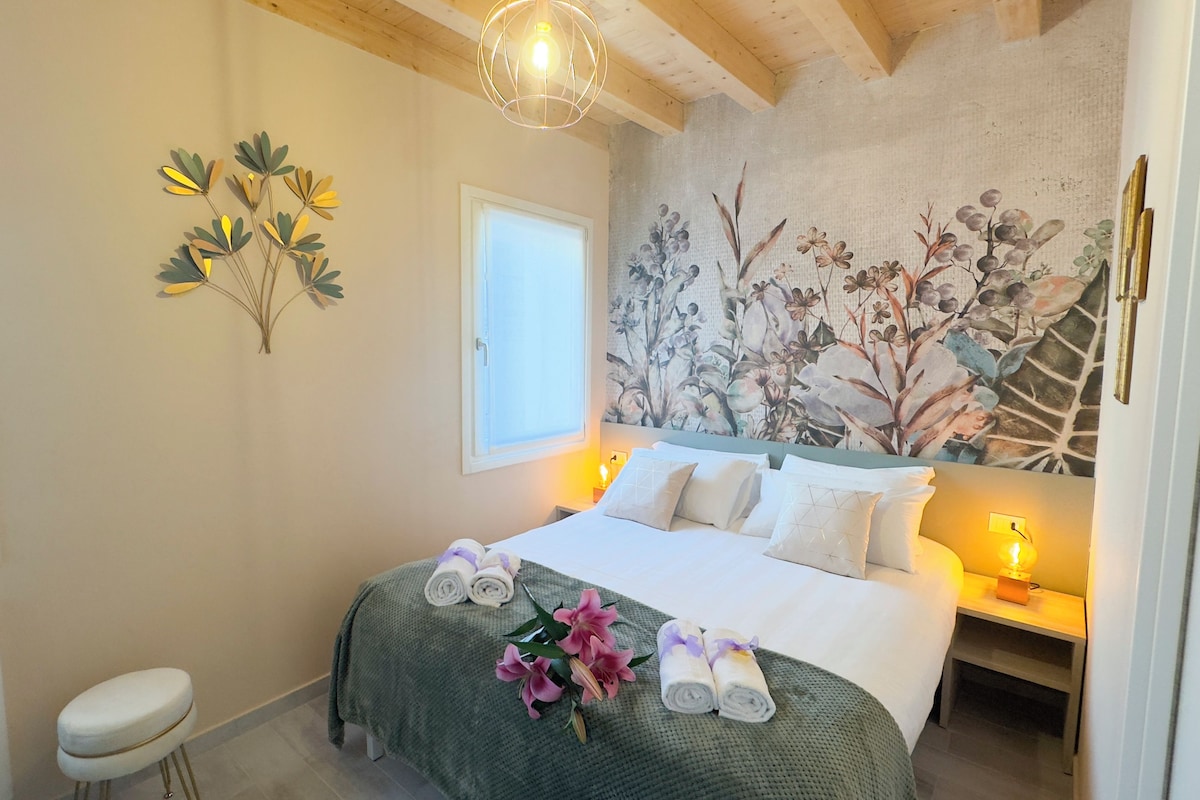 Ein Schlafzimmer mit einem Bett, Kissen, einem Nachttisch, einer Wanddekoration und einem Fenster.
