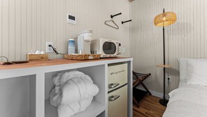 A hotel room with a kitchenette, a microwave, a coffee maker, a hanging light fixture, a bed, and a robe. - Serene 1-bedroom treehouse cabin with AC in the LBJ Grasslands (Alvord)