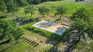 An aerial view of a green field with a concrete structure, surrounded by trees and vegetation. - Serene 1-bedroom treehouse cabin with AC in the LBJ Grasslands (Alvord)