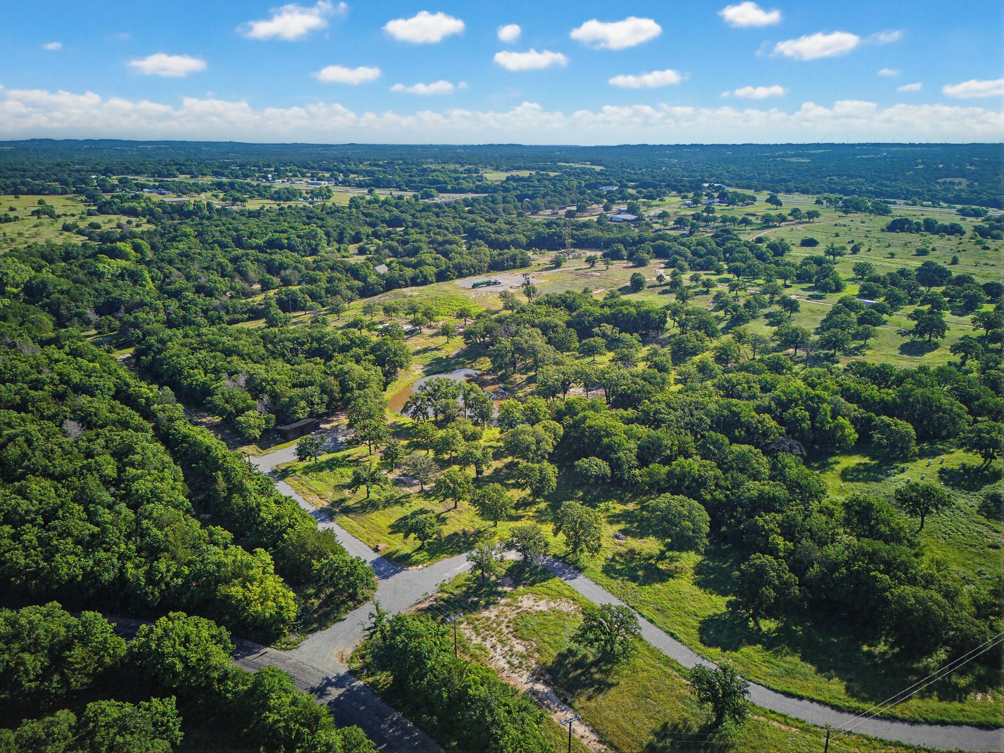 An aerial view of a lush green landscape with a winding road, trees, and open fields.