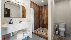 A modern bathroom with a white vanity, a large mirror, a shower with a wooden panel wall, and a toilet.