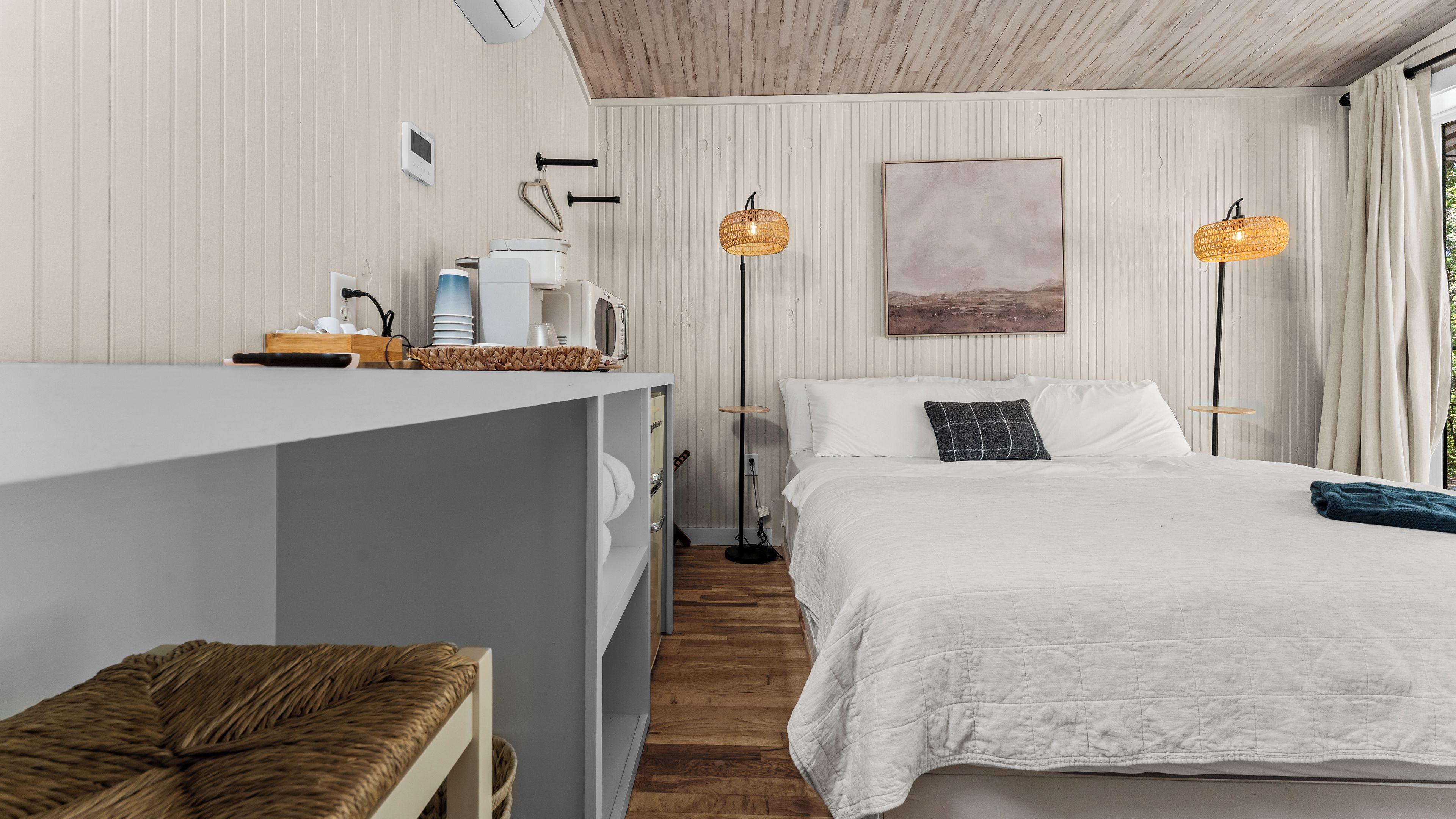 A modern bedroom with a bed, bedside tables, a desk, and two floor lamps.