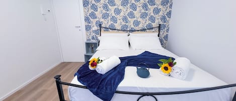 A neatly made bed with white linens, a blue throw blanket, and decorative towels with sunflowers and roses.