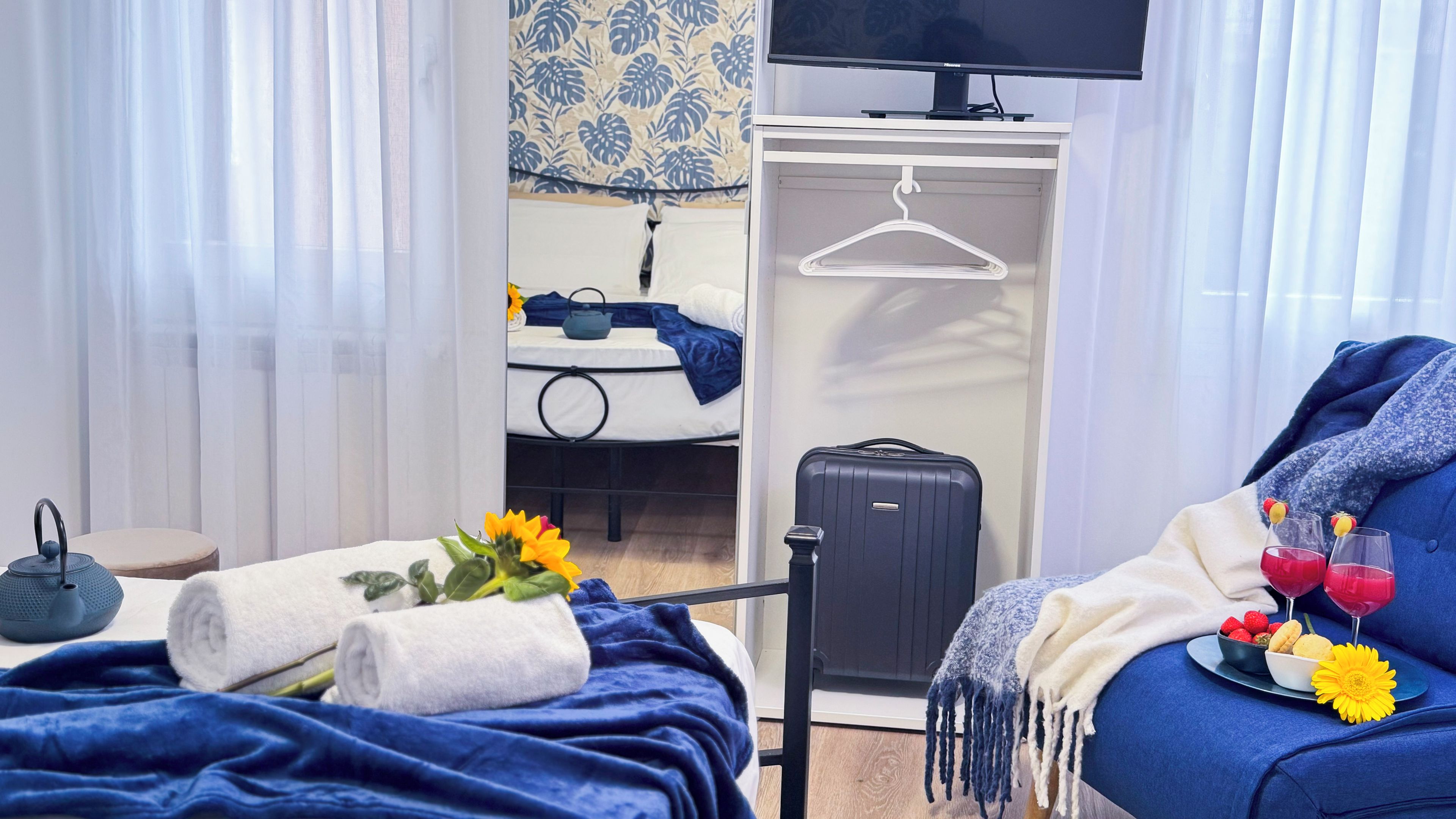 A hotel room with a bed, a suitcase, a TV, and a tray with fruit and drinks.