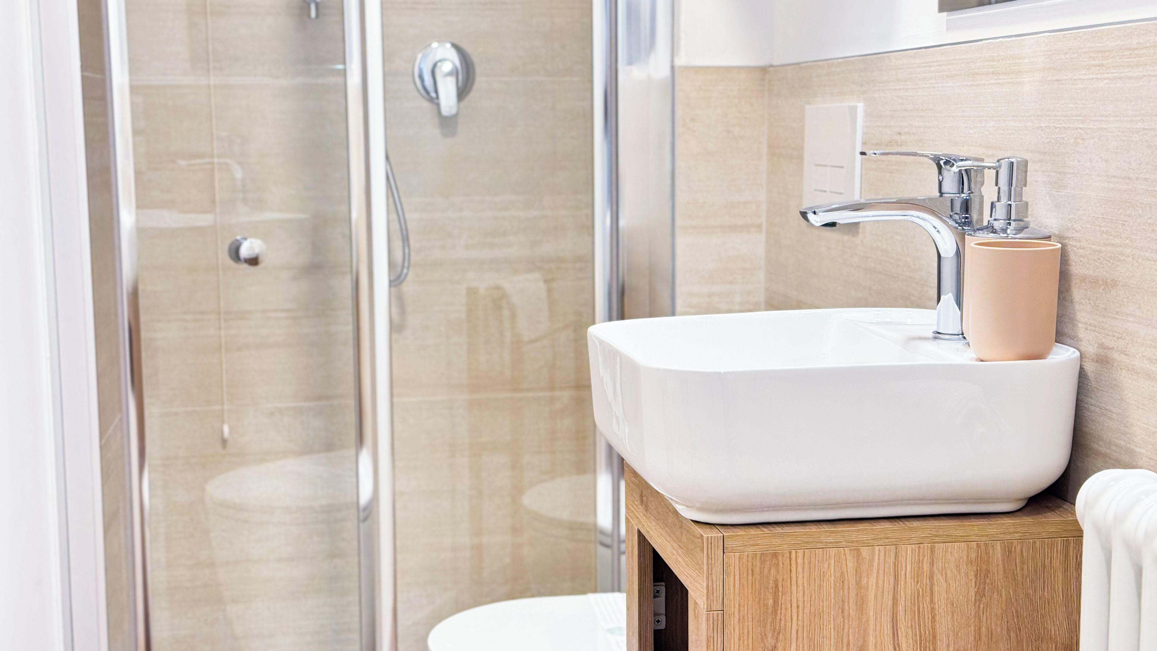 Une salle de bain moderne avec une douche à parois de verre, un lavabo blanc doté d’un distributeur de savon beige et un meuble-lavabo en bois.