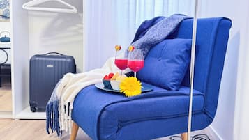 A blue armchair with a white throw blanket, a black suitcase, and a tray with a yellow flower, strawberries, and two glasses of red drink.