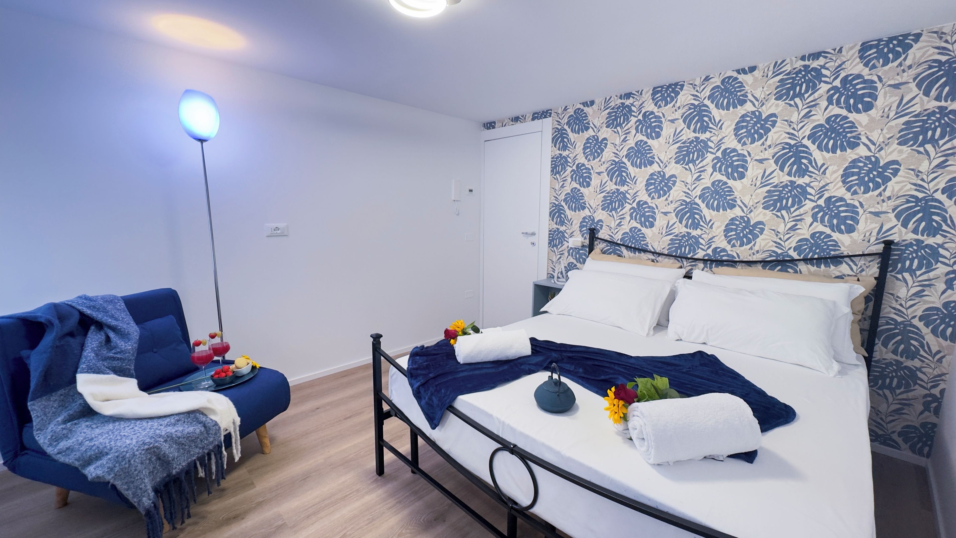 A bedroom with a bed, a chair, and a bedside table with a lamp.