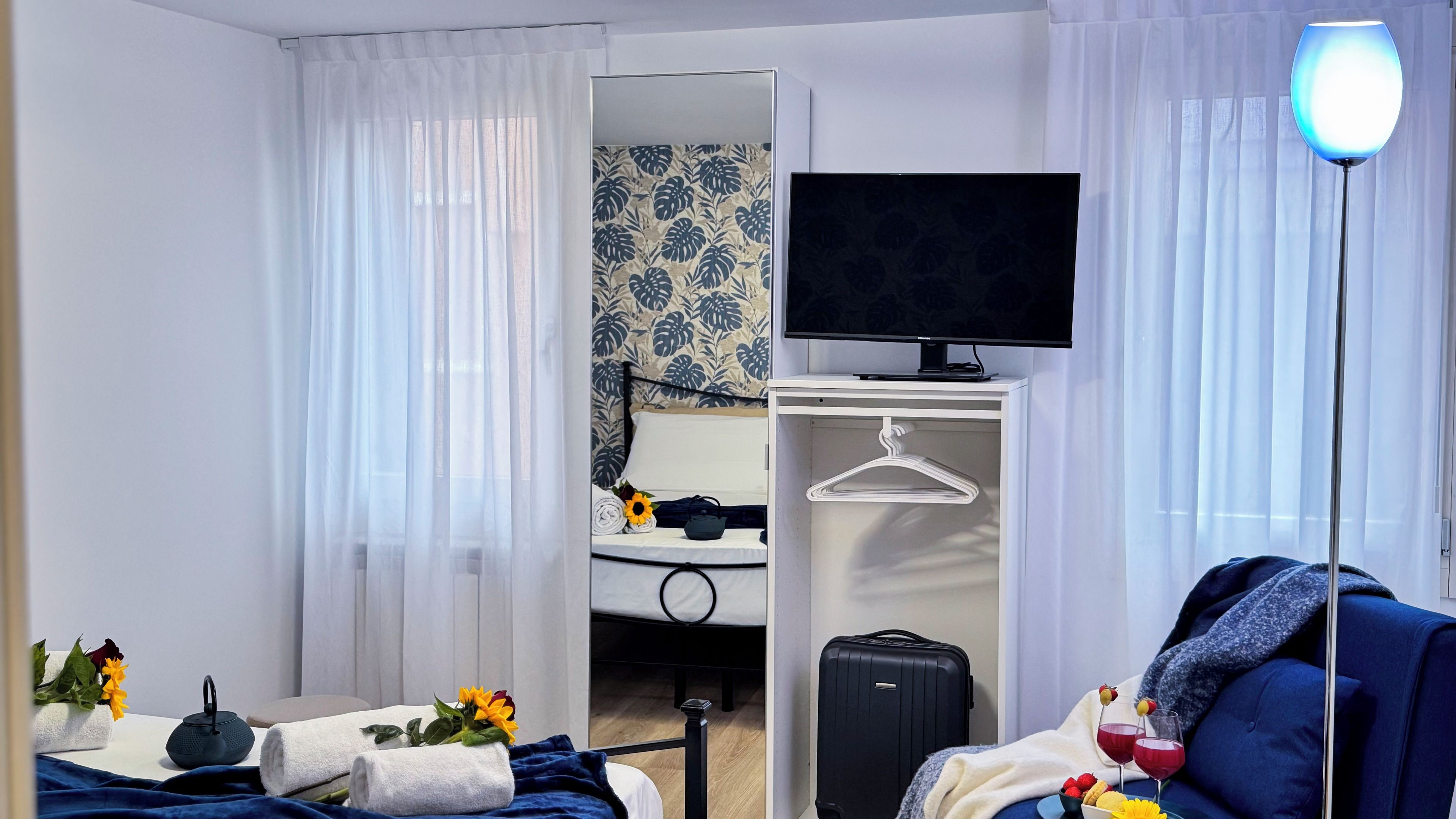 Hotelkamer met een bed, televisie, kast, koffer en nachtkastje met waterkoker en bloemen.