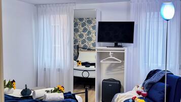 Hotelkamer met een bed, televisie, kast, koffer en nachtkastje met waterkoker en bloemen.