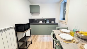 A compact kitchen with a microwave on a shelf, a sink, and a dining area with a table set for two. - Tre Esse by Ca-sa Check (Chioggia)