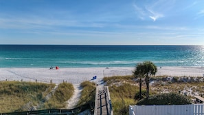 Ein Strand mit einer Holzpromenade, die zum Ufer führt, feinem Sand und einem strahlend blauen Himmel.