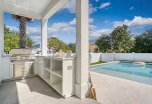 Ein Außenküchenbereich mit Grill, Pool und überdachter Sitzgelegenheit.