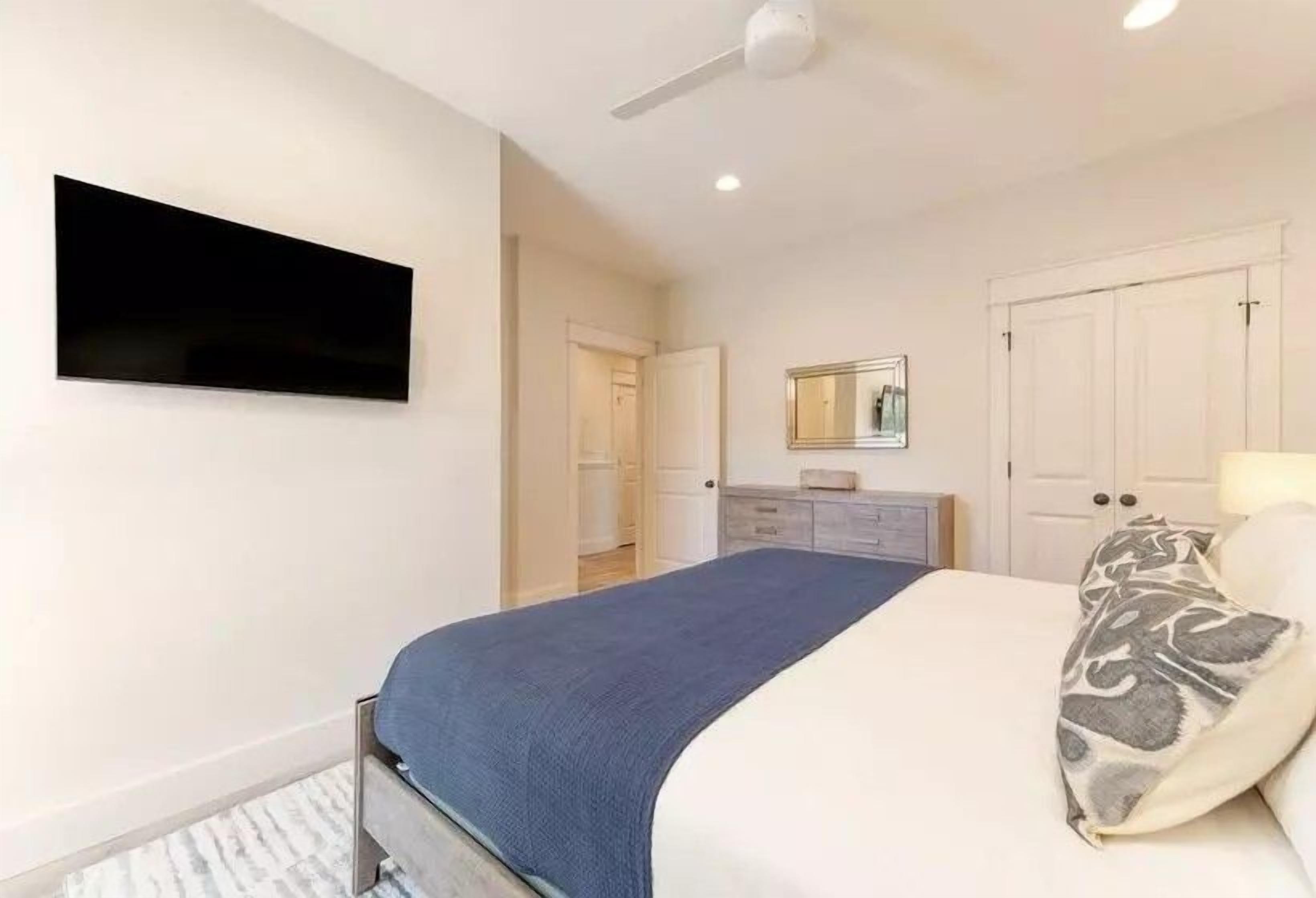 Ein Schlafzimmer mit einem Bett, einem an der Wand befestigten Fernseher, einem Deckenventilator und einem Kleiderschrank.