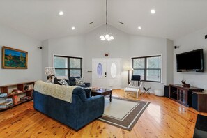 A spacious living room with a blue sofa, a television, and a fireplace. - "TreeHouse" | Hot Tub | River Access | 20m to SNP (Front Royal)