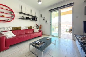A living room with a red sofa, a glass coffee table, and a sliding glass door leading to an outdoor balcony. - Family Resort Getaway with Pool Sleeps 6 (Paralimni)