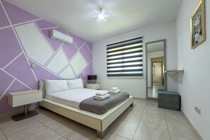 A modern bedroom with a bed, nightstands, a mirror, and a window with blinds. - Family Resort Getaway with Pool Sleeps 6 (Paralimni)