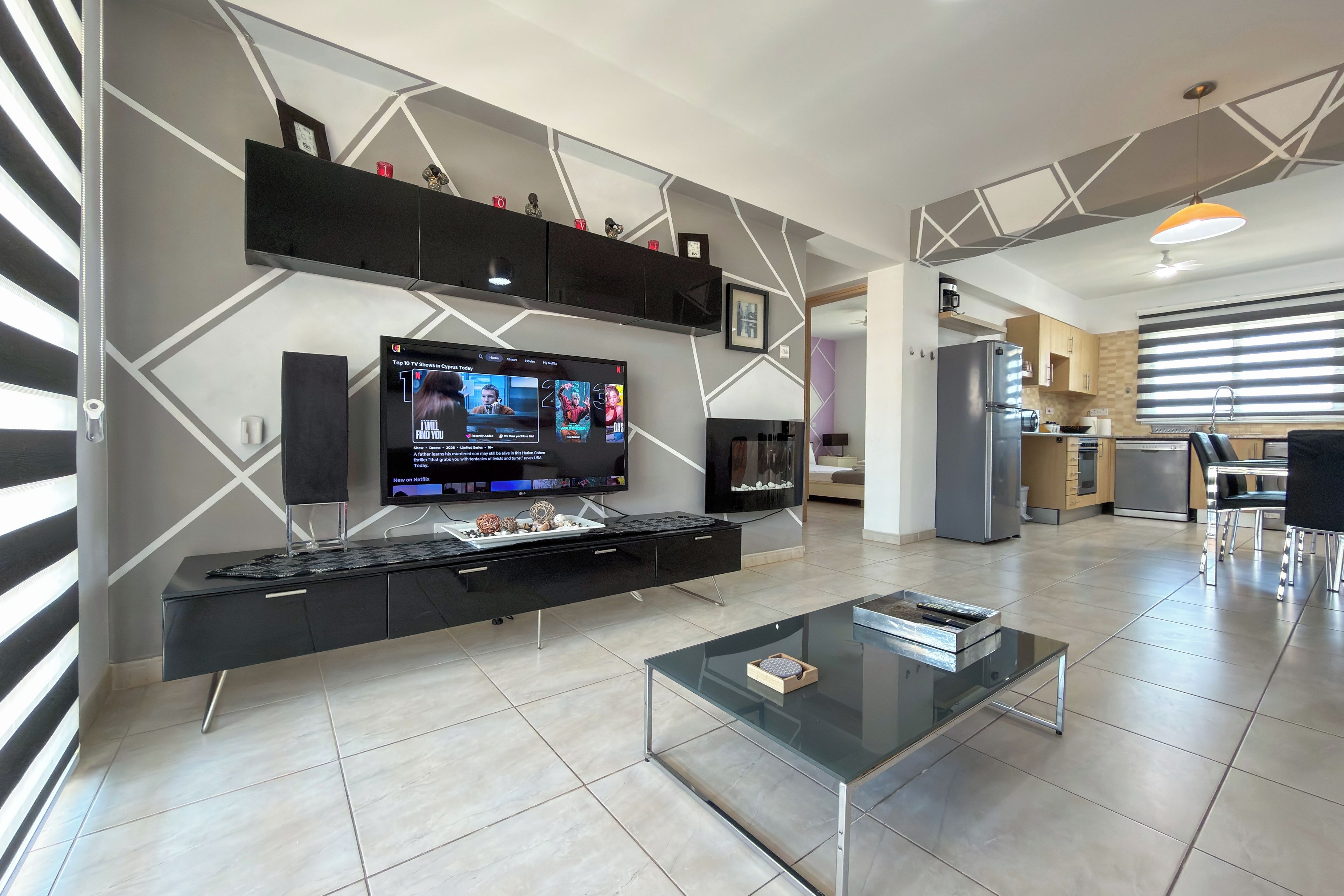 Una sala de estar moderna con un televisor de pantalla plana, una mesa de centro de vidrio y una cocina al fondo.