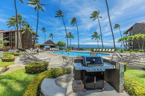 A poolside area with lounge chairs, a barbecue grill, and palm trees. - Ocean View Maui Studio Papakea C204 Near Kaanapali Beach (Lahaina)