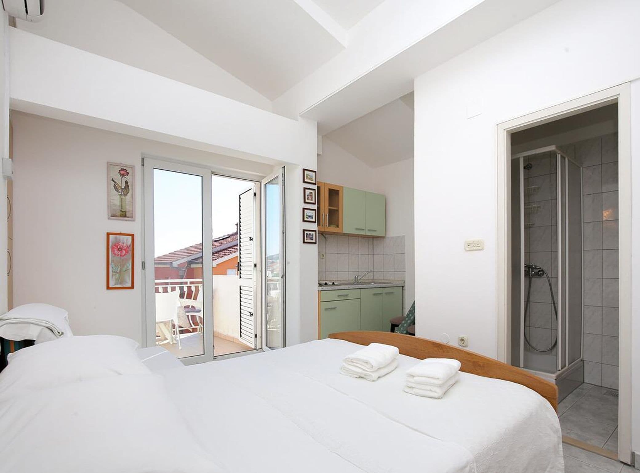 A hotel room with a bed, a bathroom with a shower, and a balcony.