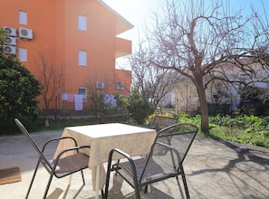 An outdoor seating area with a table and chairs, a tree, and a building in the background. - Apartments & Room Fabijan (Podstrana)