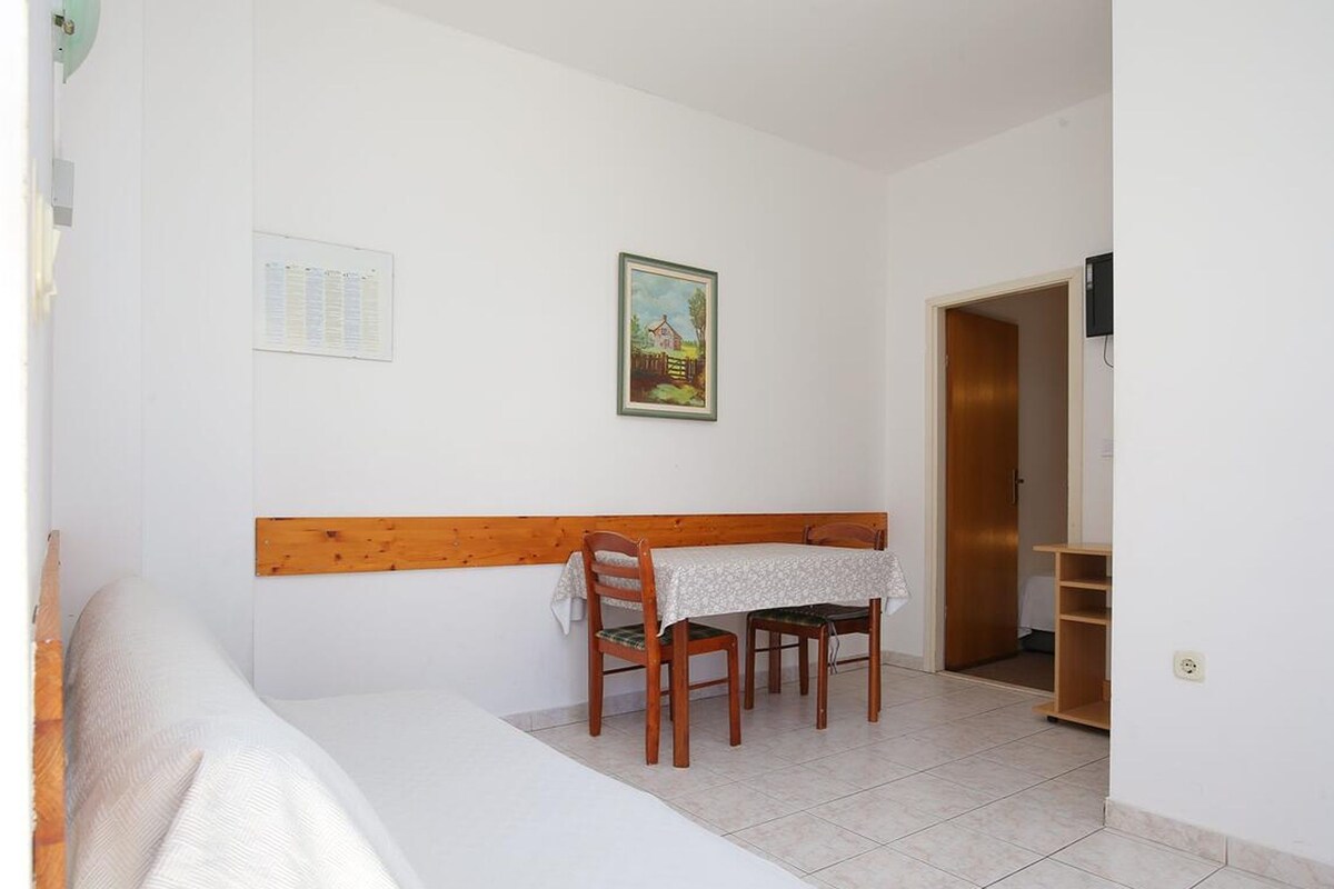 Una habitación con una cama, una mesa con sillas, un cuadro en la pared y un cabecero de madera.