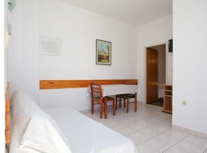 A room with a bed, a table with chairs, a painting on the wall, and a wooden headboard. - Apartments & Room Fabijan (Podstrana)