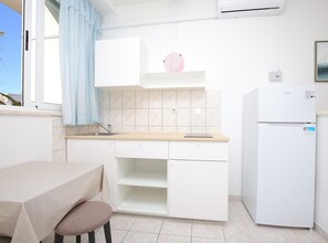 A compact kitchen with a sink, a countertop, a refrigerator, and a dining area with a table and chair. - Apartments & Room Fabijan (Podstrana)