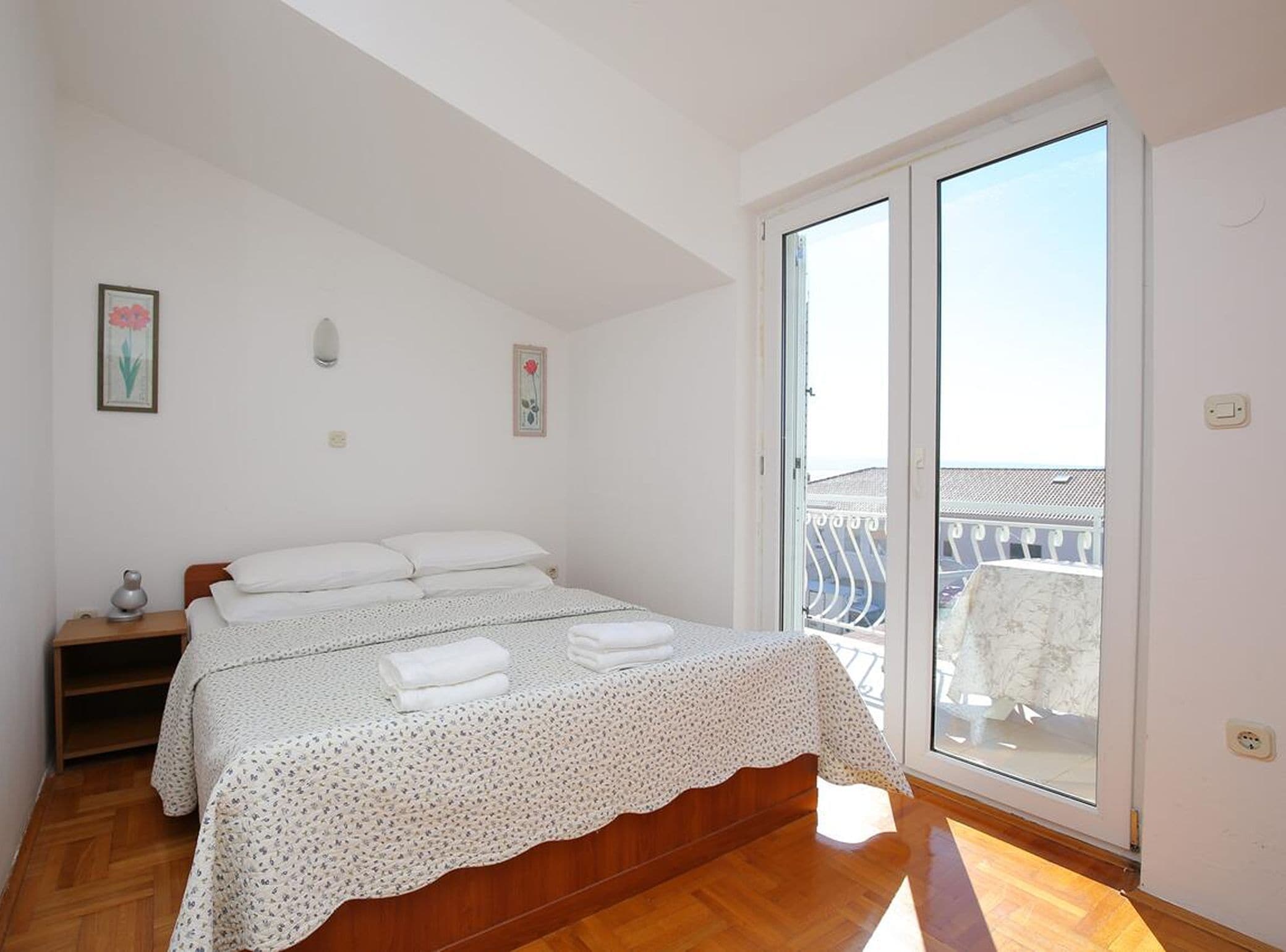 A bedroom with a bed, a nightstand, a window with a view, and a door.