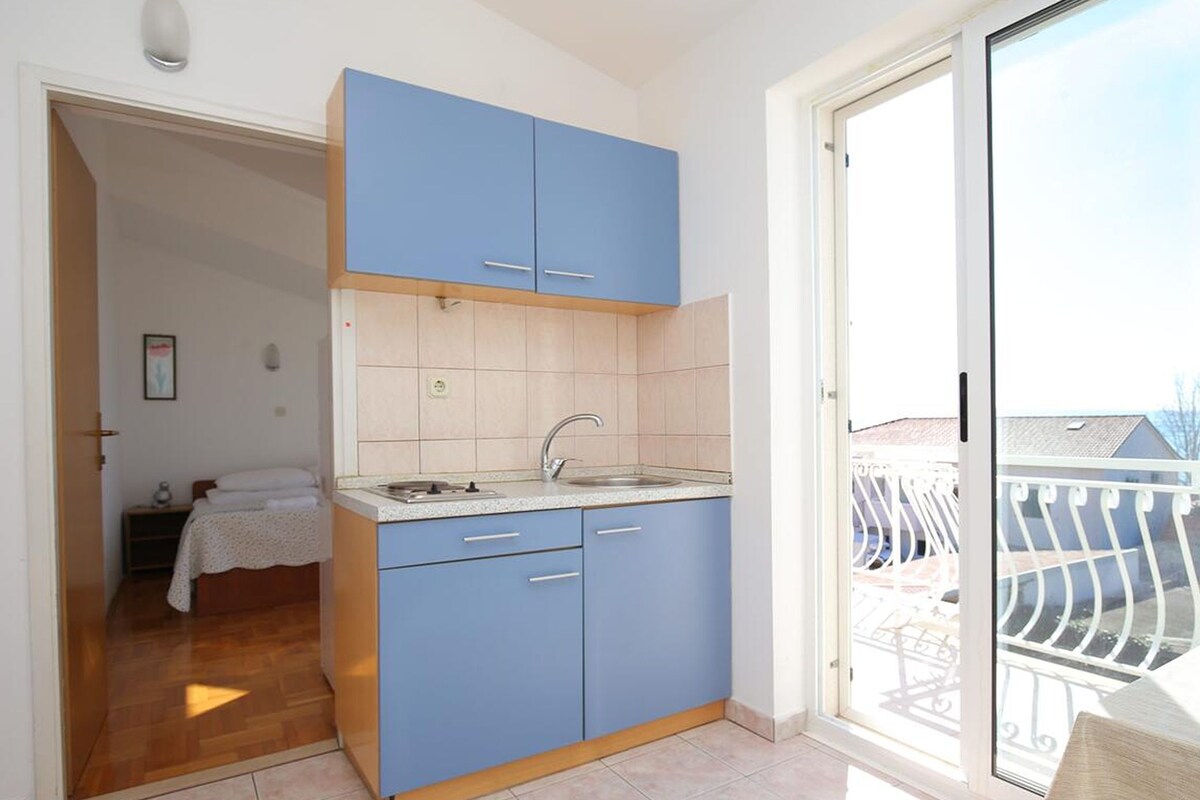 Una cocina pequeña con armarios azules, un lavamanos y un ventanal con vistas a un balcón.