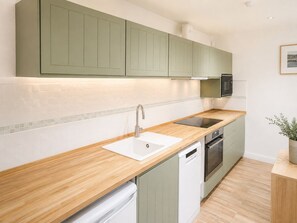 Una cocina moderna con armarios verde claro, encimera de madera, lavavajillas integrado y microondas.