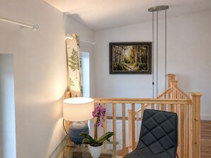 A modern interior with a wooden staircase, a framed forest painting, a lamp, and a potted orchid. - Riber Nest Cottage - Matlock - Hot Tub - Sleeps 4 (Starkholmes)