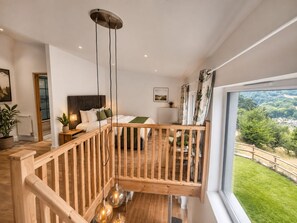 A modern bedroom with a large bed, a wooden staircase, and a view of the outdoors. - Riber Nest Cottage - Matlock - Hot Tub - Sleeps 4 (Starkholmes)