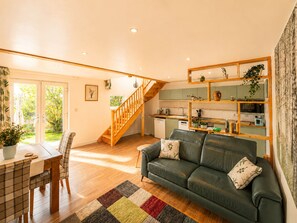 A spacious living area with a wooden staircase, a green sofa, and a kitchen with green cabinets. - Riber Nest Cottage - Matlock - Hot Tub - Sleeps 4 (Starkholmes)