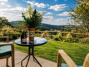 A round table with a bottle and a potted plant on it, set on a patio with a view of a countryside landscape. - Riber Nest Cottage - Matlock - Hot Tub - Sleeps 4 (Starkholmes)