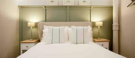 Una cama bien hecha con sábanas blancas y rayas azules, dos mesitas de noche con lámparas y un cabecero con tres pequeños marcos de fotos.