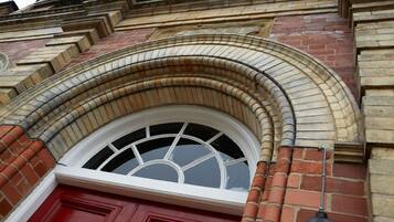 A red door with a white-framed window, brickwork, and a curved stone arch above it.