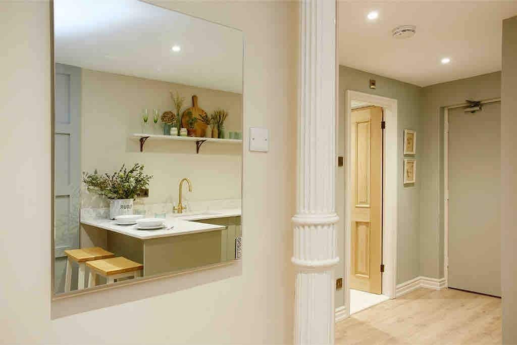 A bathroom with a large mirror, a sink, and a toilet. There is a wooden stool and a plant on the counter.
