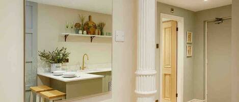 A bathroom with a large mirror, a sink, and a toilet. There is a wooden stool and a plant on the counter.