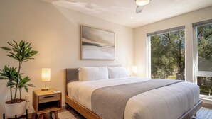 Una camera da letto con un letto, comodini, una ventola a soffitto, una finestra vista alberi e un quadro al muro.
