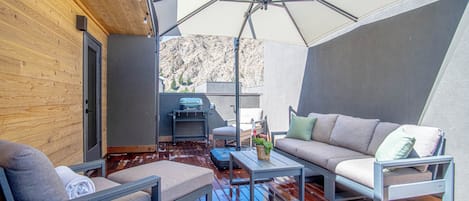 Un espace extérieur moderne, aménagé avec une terrasse en bois, un grand parasol et offrant une vue sur un paysage montagneux.