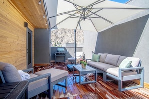 A modern outdoor seating area with a wooden deck, a large umbrella, and a view of a mountainous landscape. - River Street Lookout - Lux 3BD w/ Rooftop Views + Hot tub - Downtown Hailey (Hailey)