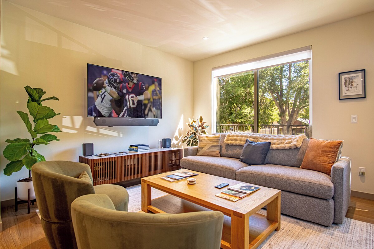 Uma sala de estar moderna com TV de tela plana, sofá, mesa de centro e uma janela grande.