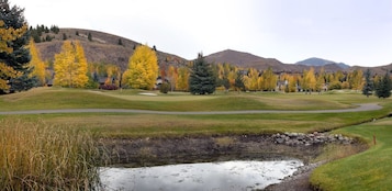 Un campo de golf con un estanque, árboles y un paisaje colinas al fondo.